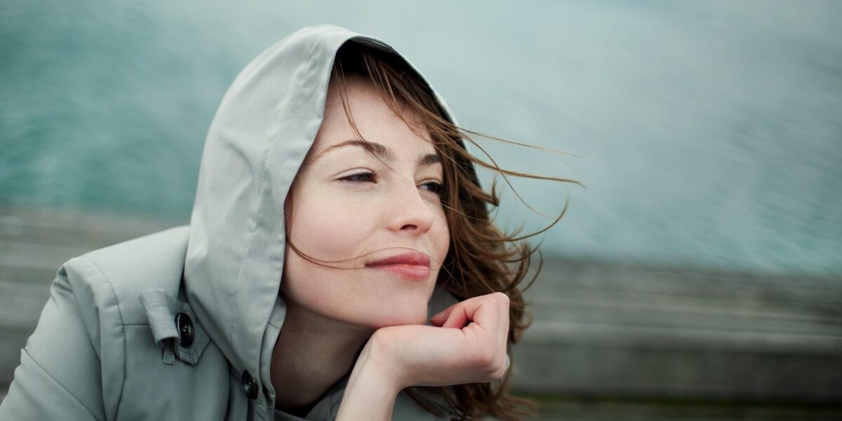 Junge Frau mit Anorak blickt glücklich in die Ferne.