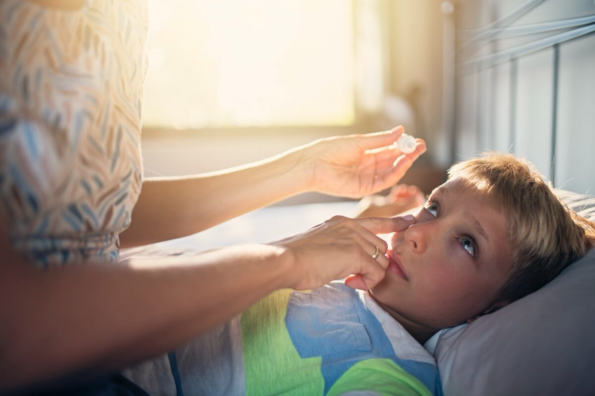 Junge liegt im Bett und erhält Augentropfen.