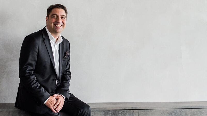 Prof. Dr. Hakan Kaymak sitzt auf einem modernen Sideboard in seiner Praxis.