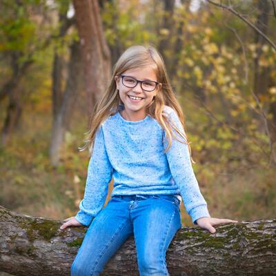Schülerin mit Brille sitzt auf einem Baumstamm im Wald.