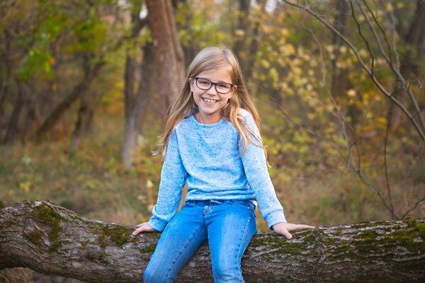 Schülerin mit Brille sitzt auf einem Baumstamm im Wald.